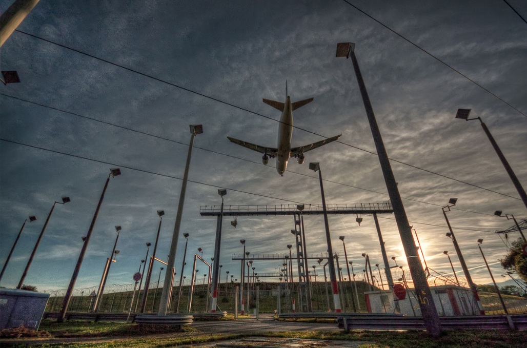 Un gran avión comercial volando sobre la infraestructura eléctrica de un aeropuerto.